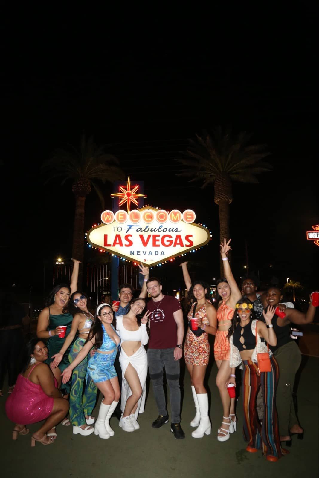 Group of friends posing in front of the Welcome to Fabulous Las Vegas sign during a private club crawl, enjoying the nightlife and wearing fun outfits